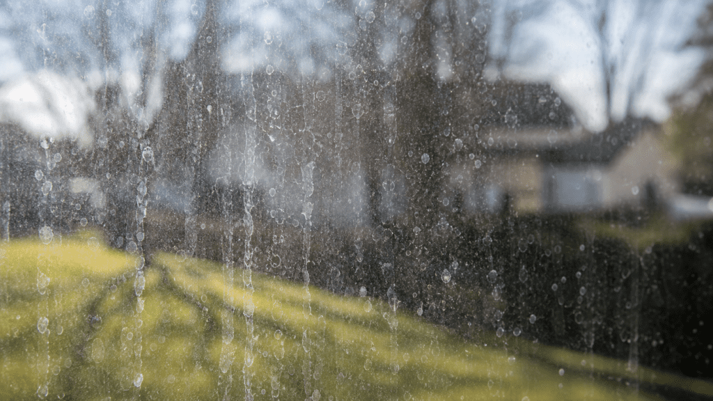 Cloudy hard-water mineral spots and stains on a residential window pane overlooking a suburban Ohio backyard
