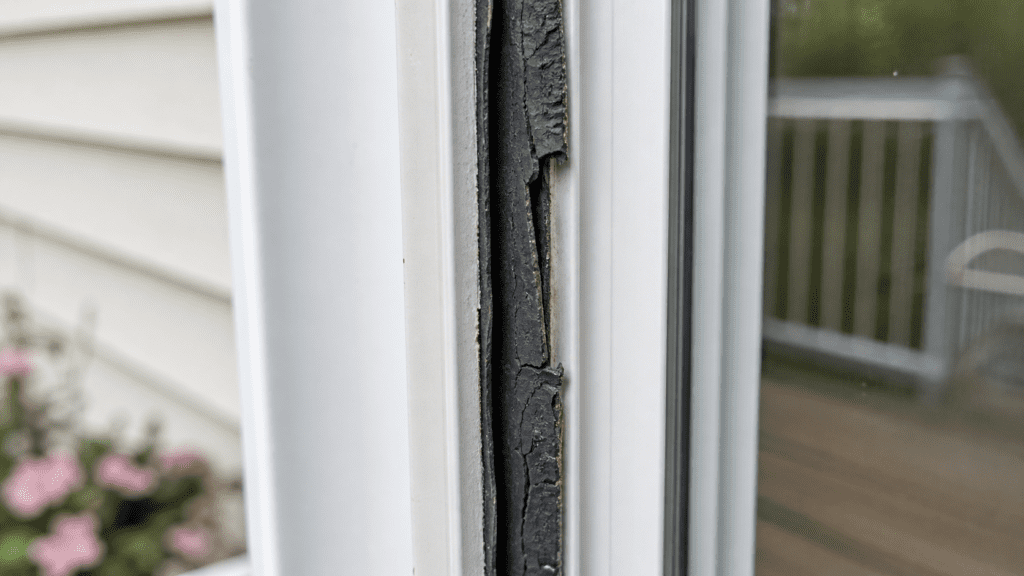 Cracked, dried-out rubber weatherstripping seal peeling away from a white sliding glass door frame at an Ohio home
