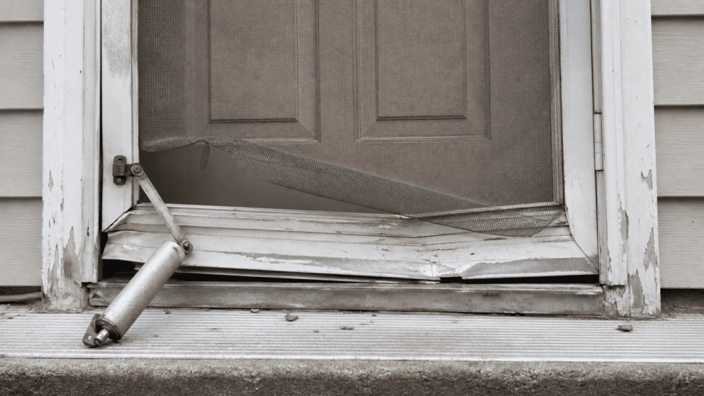 Old weather-damaged storm door with bent frame and torn screen on an Ohio home