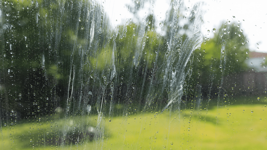 Sunlit residential window glass covered in cloudy soap streaks and water droplets with a green Ohio backyard behind it