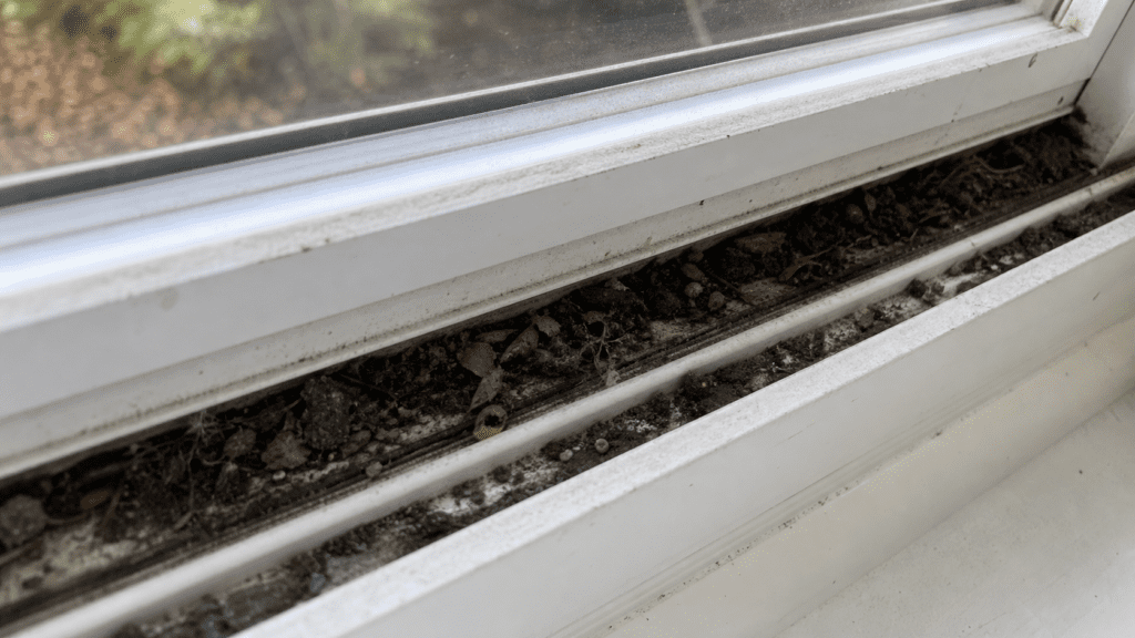 Dirty white vinyl window track packed with grime, dust and debris in a suburban Ohio home