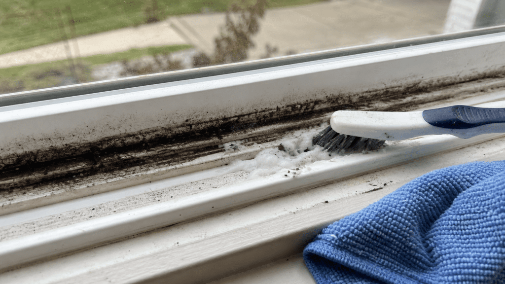 Deep-cleaning a caked window track with a scrub brush and baking soda paste in an Ohio home