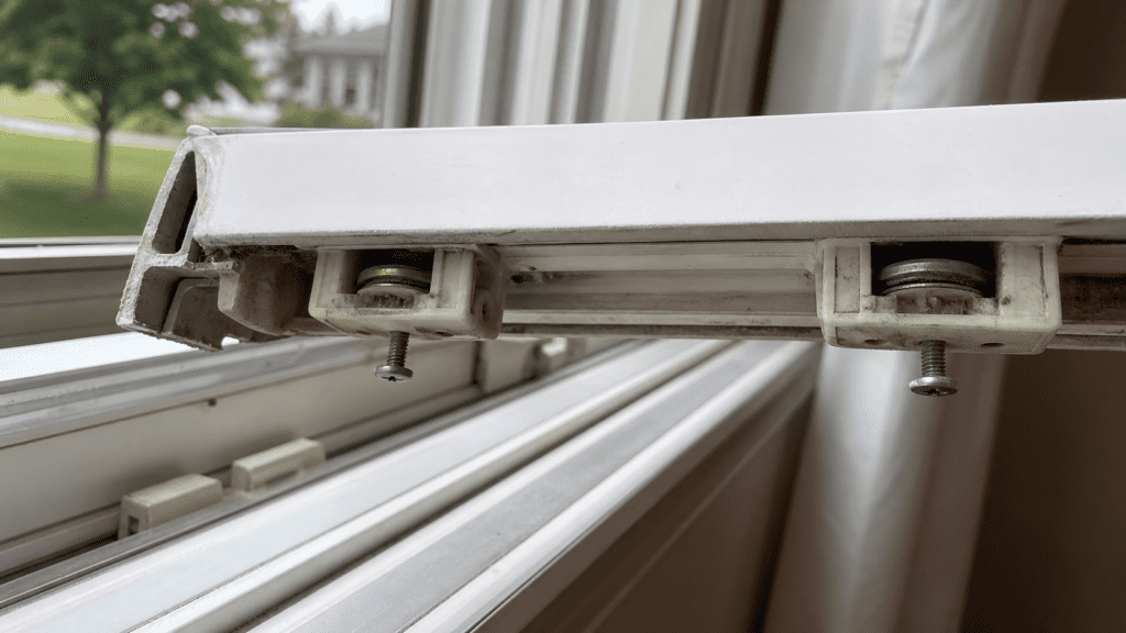 Underside of a removed sliding window sash showing worn roller wheels above the empty track in an Ohio home