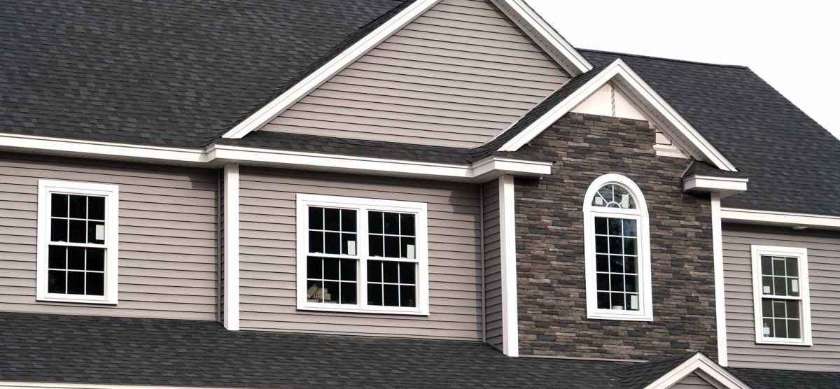 White grid-style windows, including a decorative arched window, installed on gray vinyl siding with stone accents