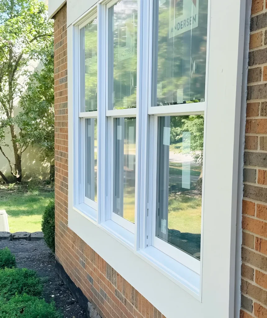 Three new white double-hung windows grouped in a brick wall with beige trim
