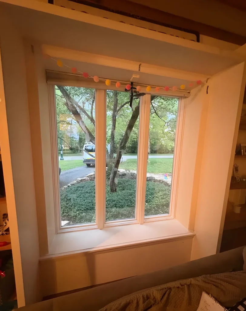 Three-light window set into a deep recess with a pom-pom garland across the top and a tree outside