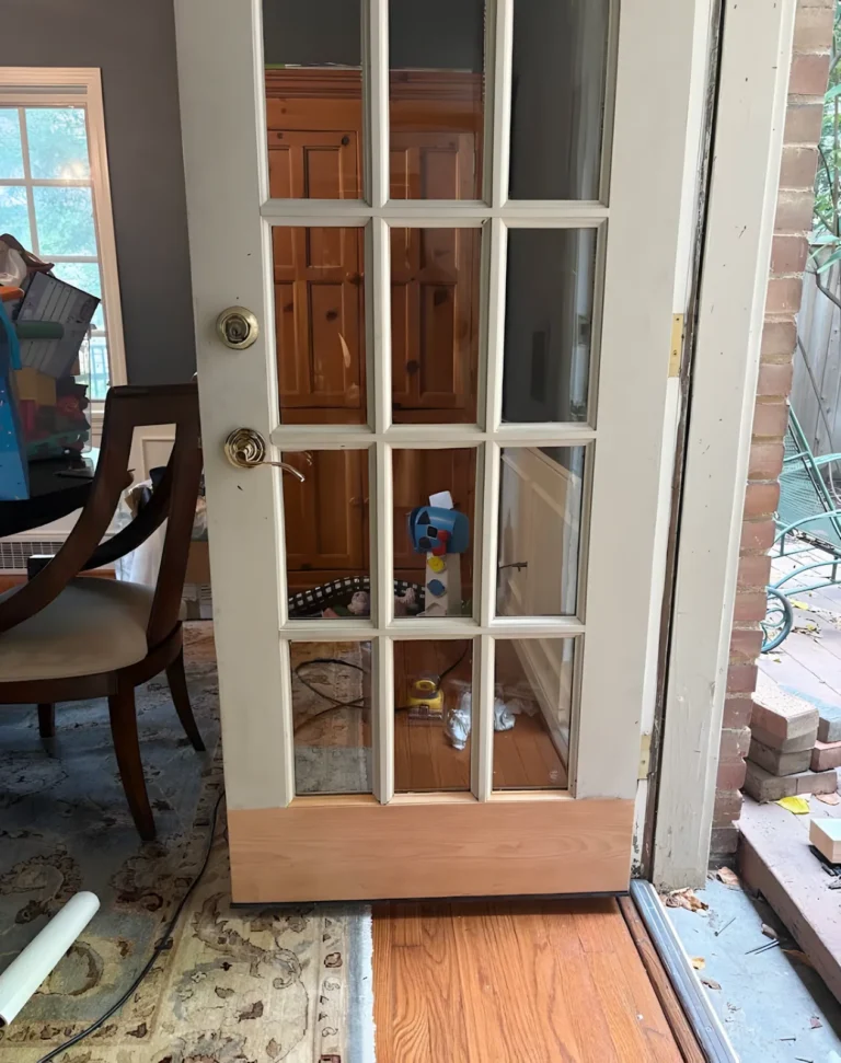 Multi-light French door with a new unpainted wood strip along the bottom rail, open onto a brick patio