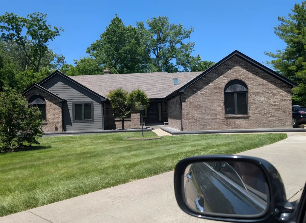 Brick ranch house with dark gray trim, black-framed windows and arched-top windows on both gables, photographed from a car