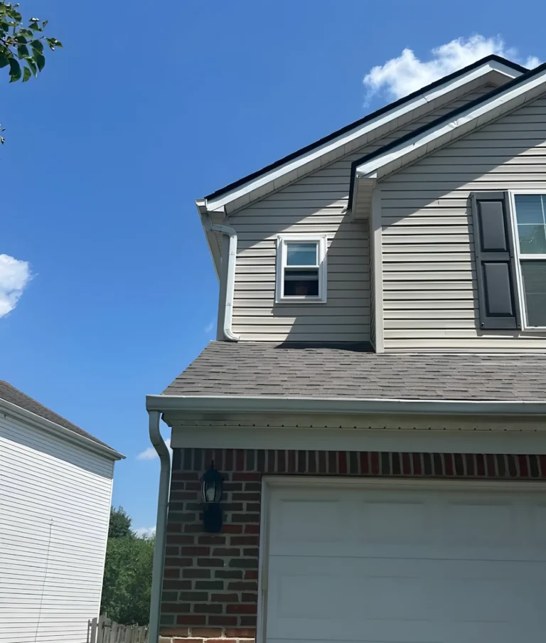 New rectangular window in the gable of a two-story house with beige siding, black shutters and a brick garage base