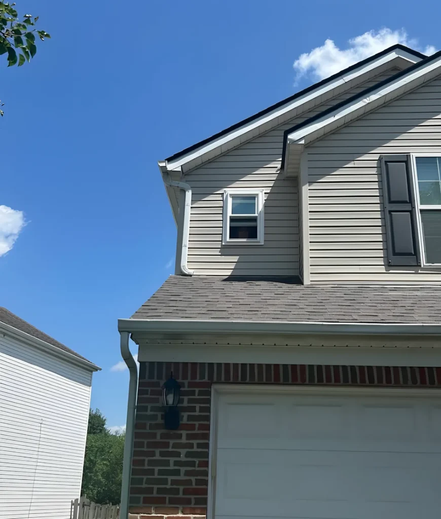 New rectangular window in the gable of a two-story house with beige siding, black shutters and a brick garage base