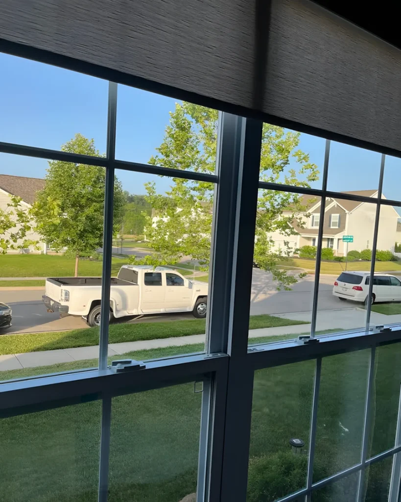 Double-hung window with divided lights and a roller shade at the top, a white pickup parked on the street outside