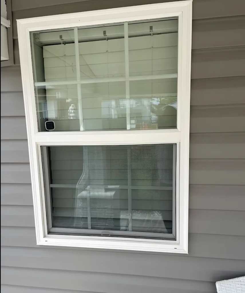 White double-hung window with a grid pattern in the upper sash, set in gray lap siding