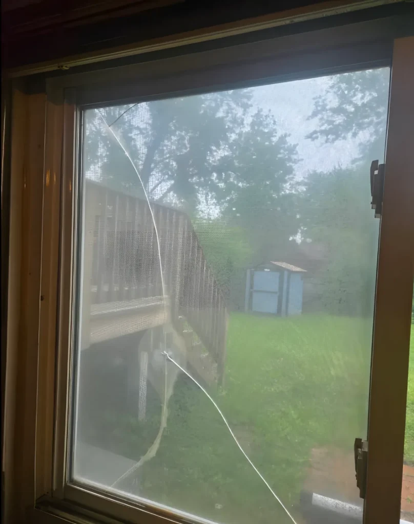Window with a long crack running through the glass, a wooden deck and a blue shed visible outside