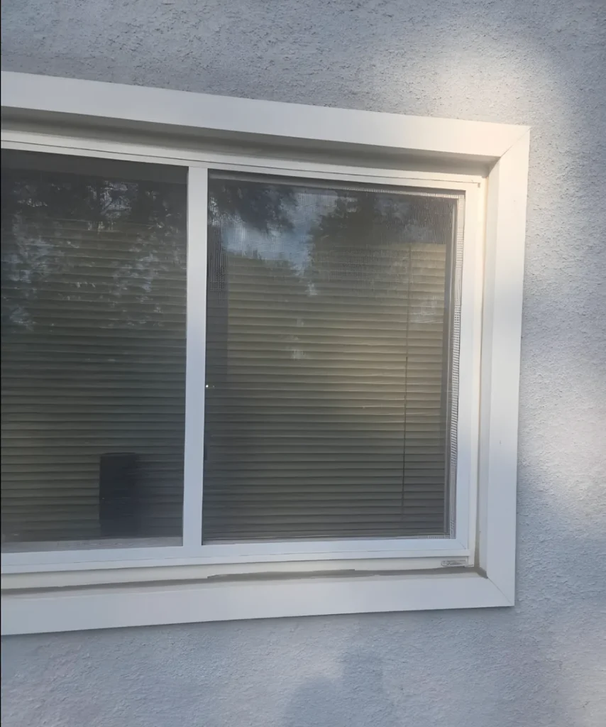 Finished window with white trim in a textured stucco wall, blinds visible behind the glass